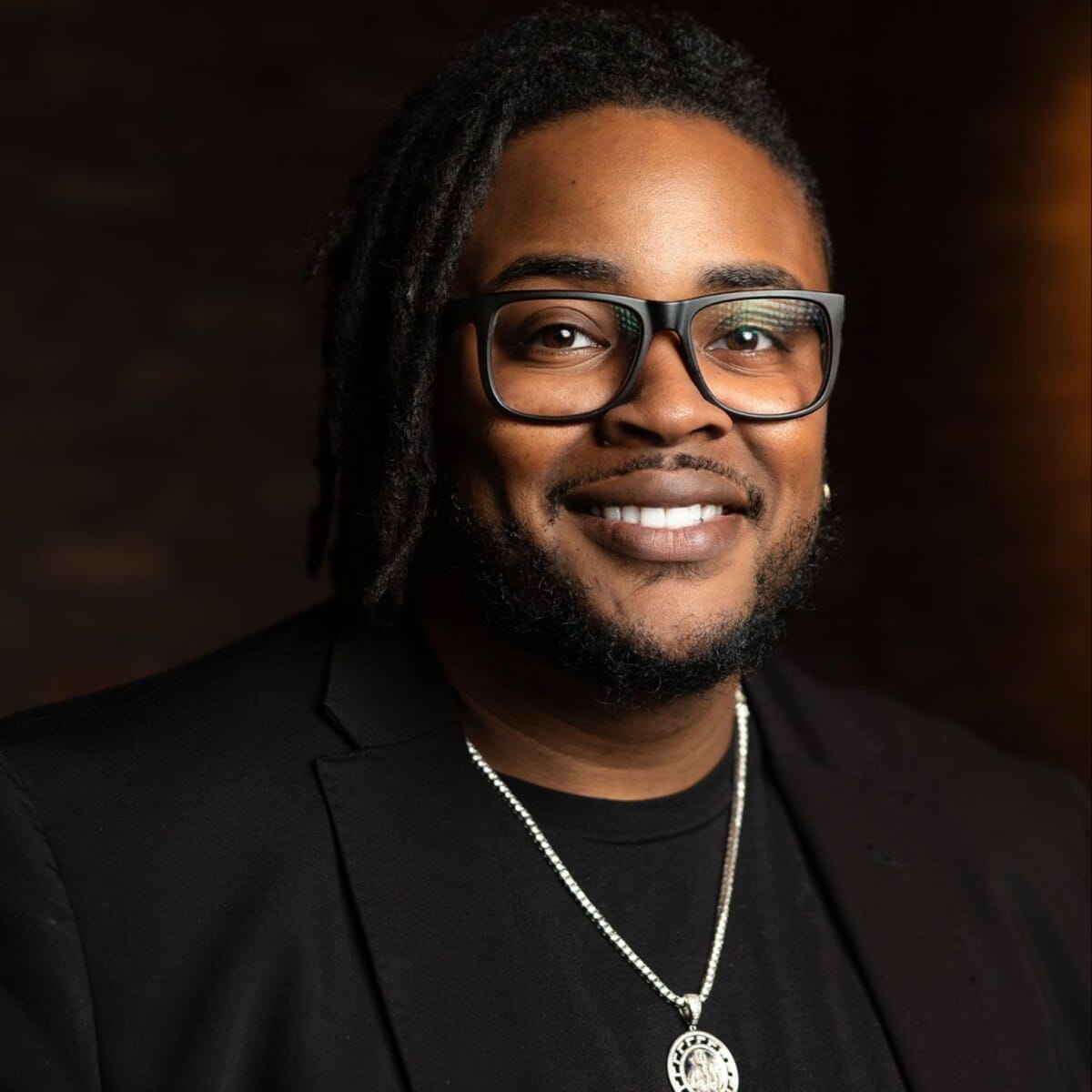 Marketing Co-founder Ken Floyd with glasses smiling in a dark background.
